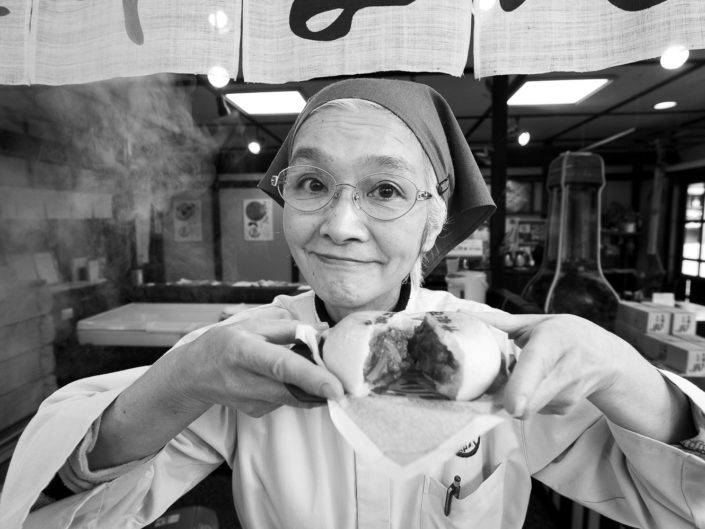 Foto Reportage in bianco e nero realizzate in Giappone, Usi e costumi di un popolo, qui in foto una locandiera offre una polpetta giapponese a Takayama